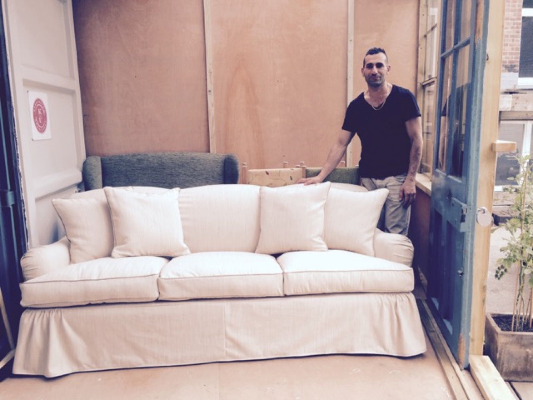 Upholsterer standing behind a finished cream sofa at the workshop entrance