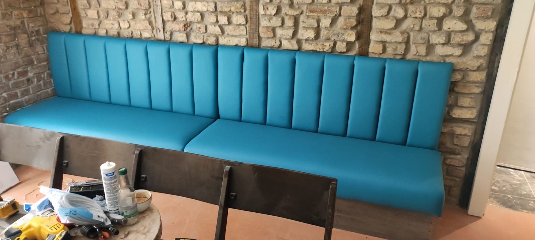 Blue vertical-channel restaurant banquette seating fitted against an exposed brick wall