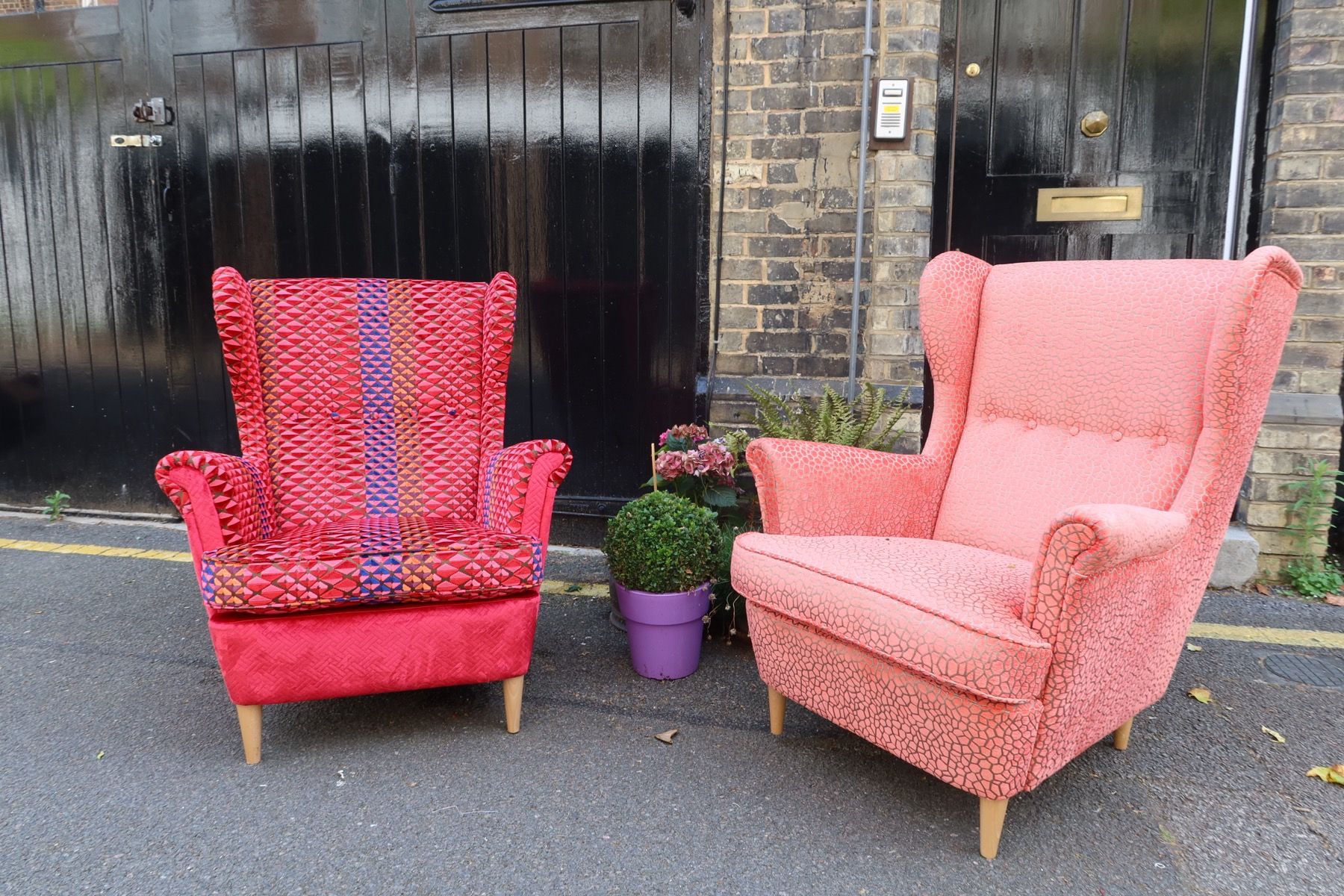 Two armchairs upholstered in pink and coral fabric outside a London upholstery workshop